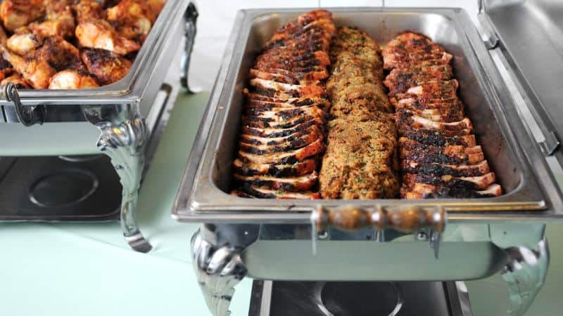 Buffet trays filled with sliced roasted meat and grilled chicken at a catered event.