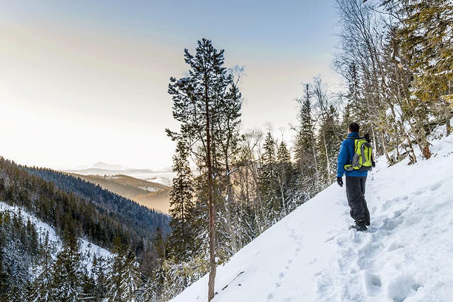 Man hiking in snow on vert steep forested mountainside