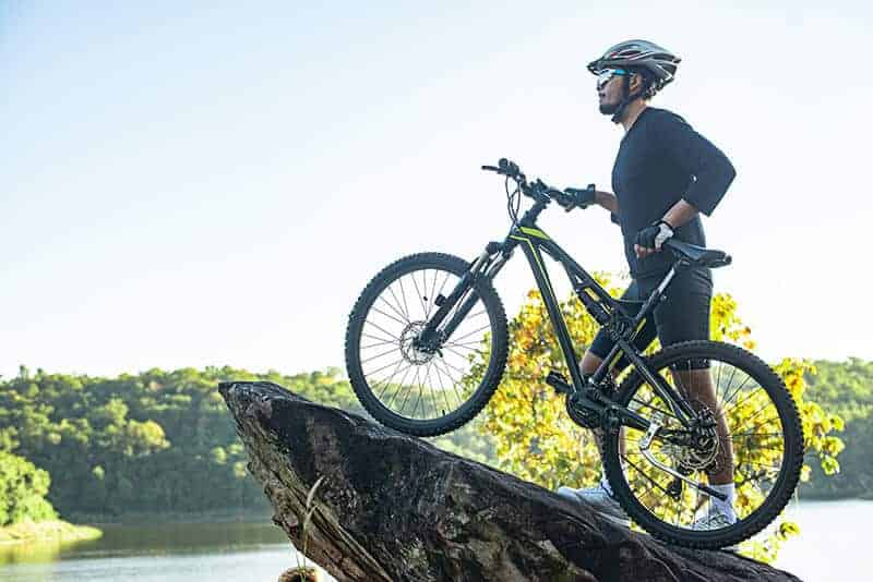 Man with mountain bike on jutting rock in front of lake