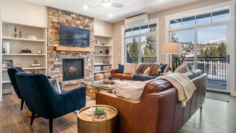 Cozy living room with a stone fireplace and large windows overlooking trees.