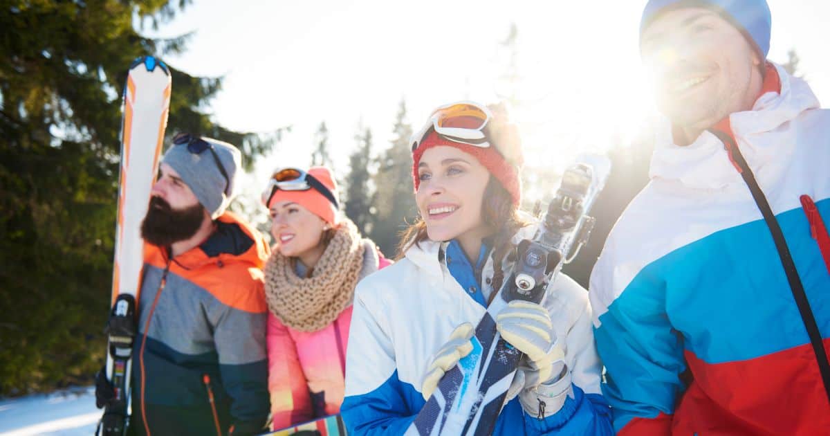 Four friends in colorful ski gear smiling with skis in hand.