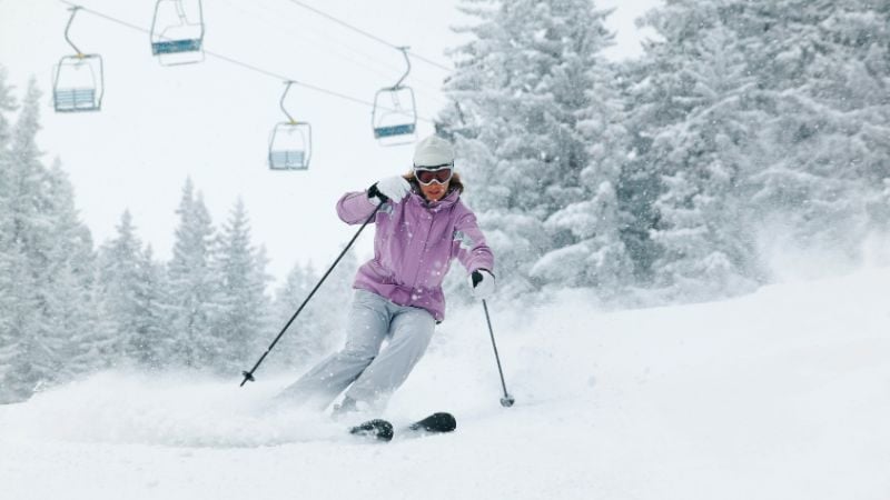 Skier in a purple jacket carving down a snowy mountain.