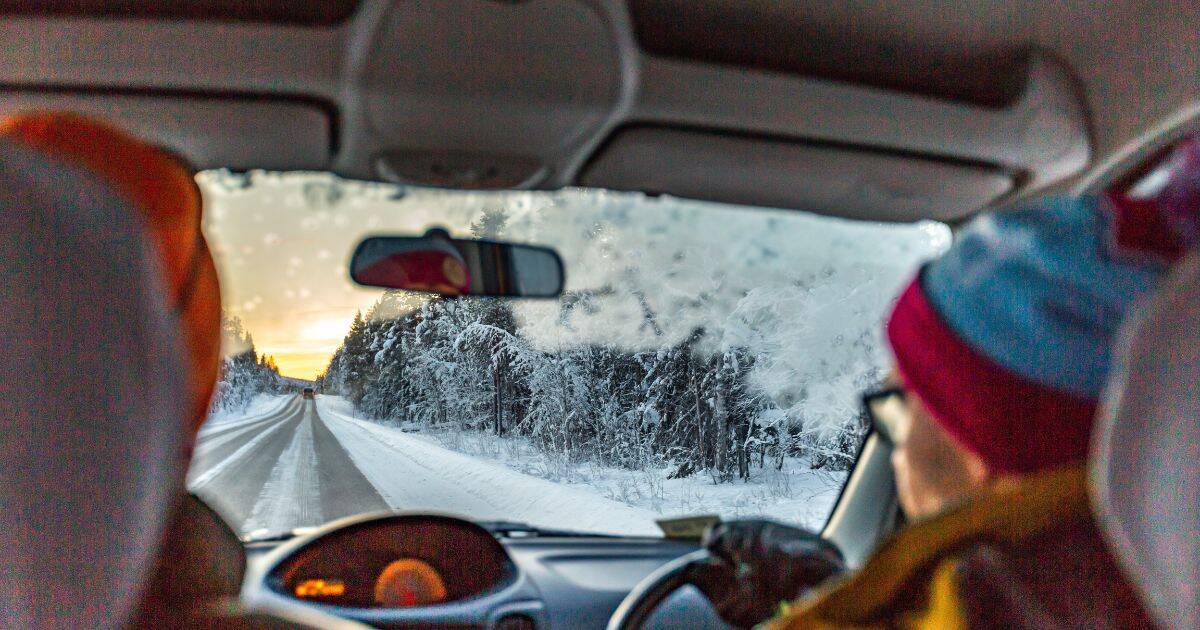 Two people driving down a snowy forest road at sunset.