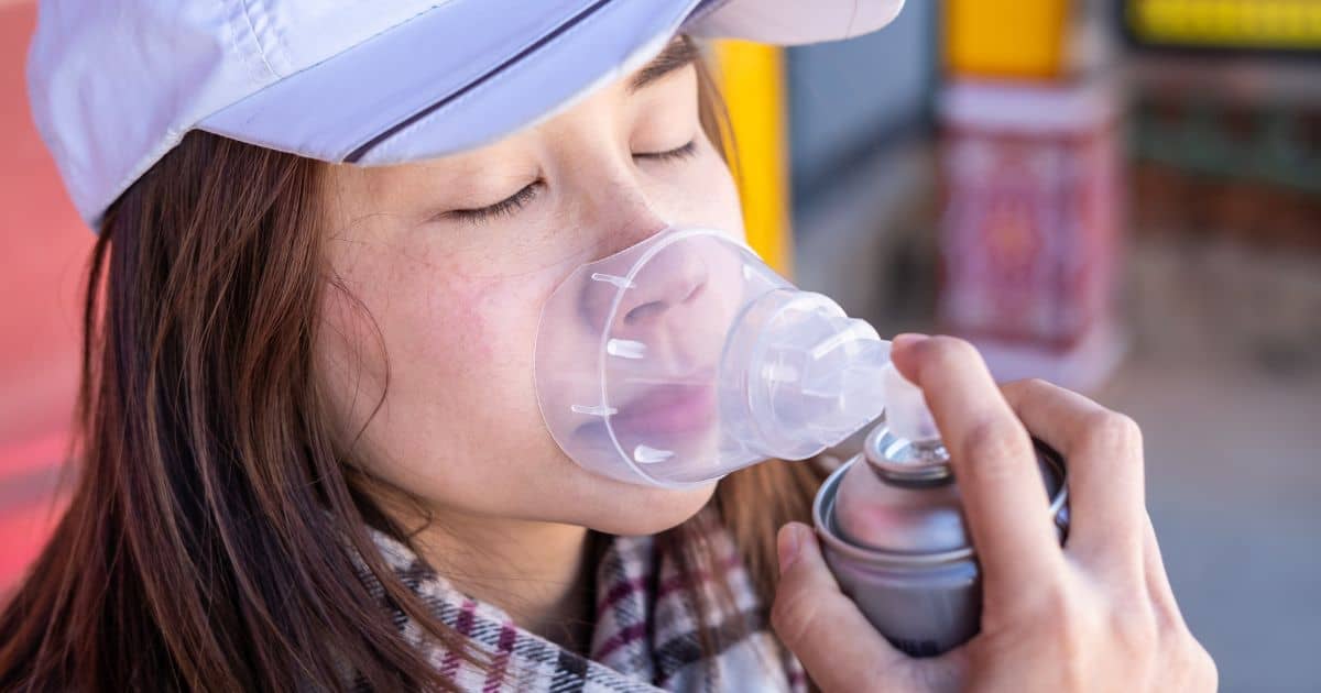 Person using an oxygen mask canister while outdoors.