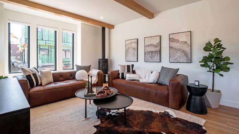 Modern living room with leather sofas, wood beams, and large windows.