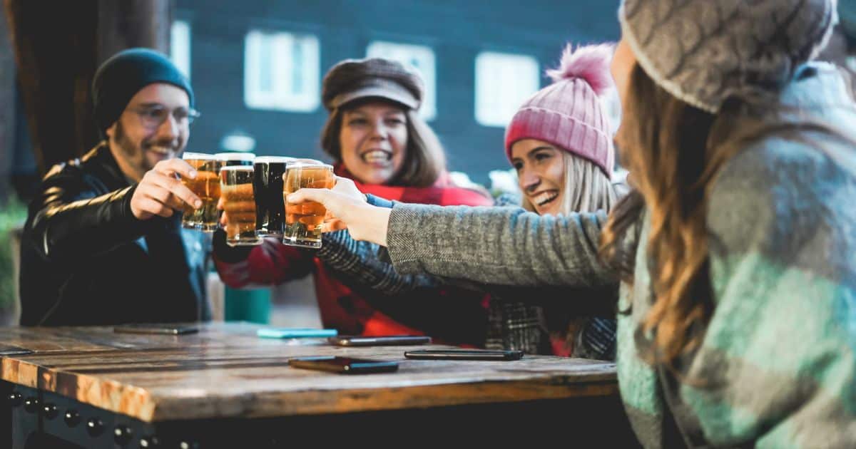 Friends clinking glasses of beer at an outdoor table in winter clothing.