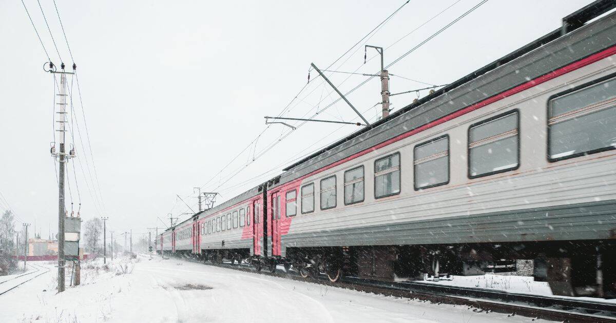 Passenger train traveling through a snowy railway corridor during winter.