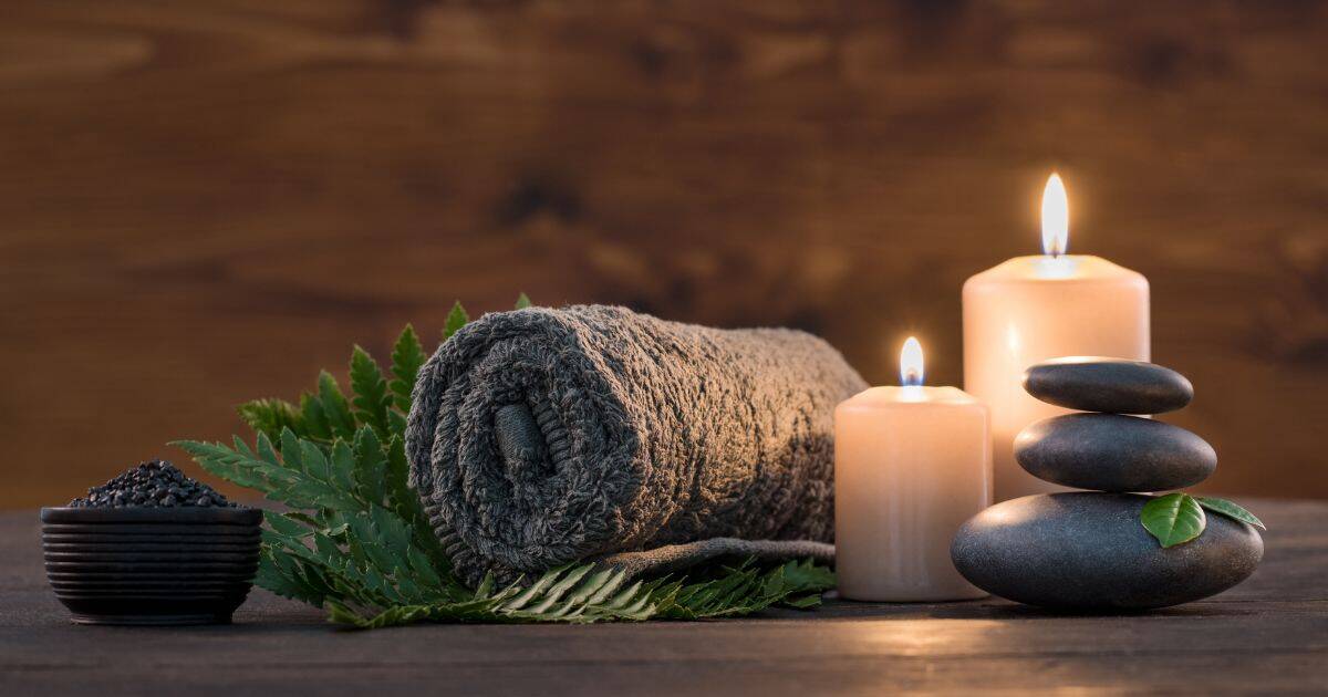 Rolled gray towel with stacked stones and lit candles on a wooden surface.