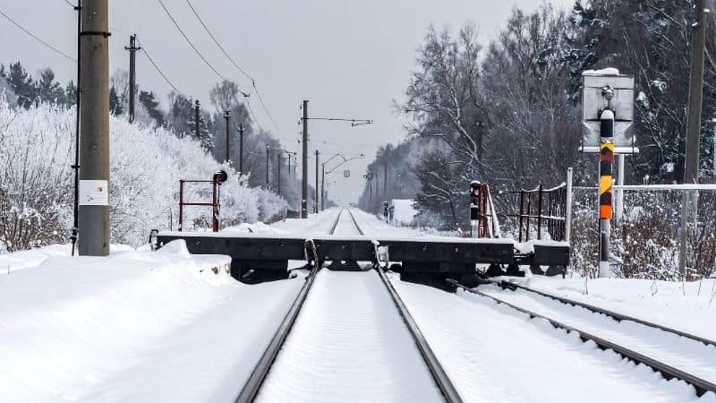 Snow-covered railroad tracks with signals and trees in a winter setting.