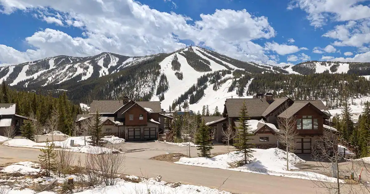 A wide view of a snowy ski mountain with large houses in the foreground.