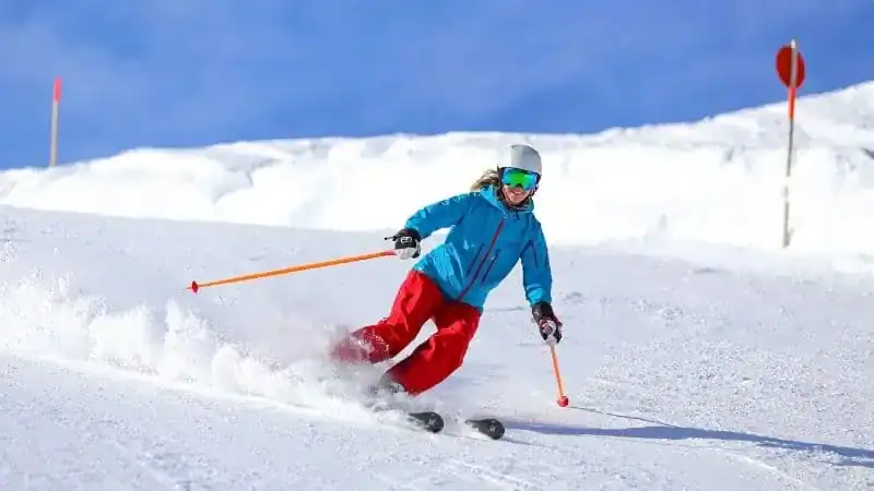 A skier wearing a blue jacket and red pants carving down a snowy ski slope.